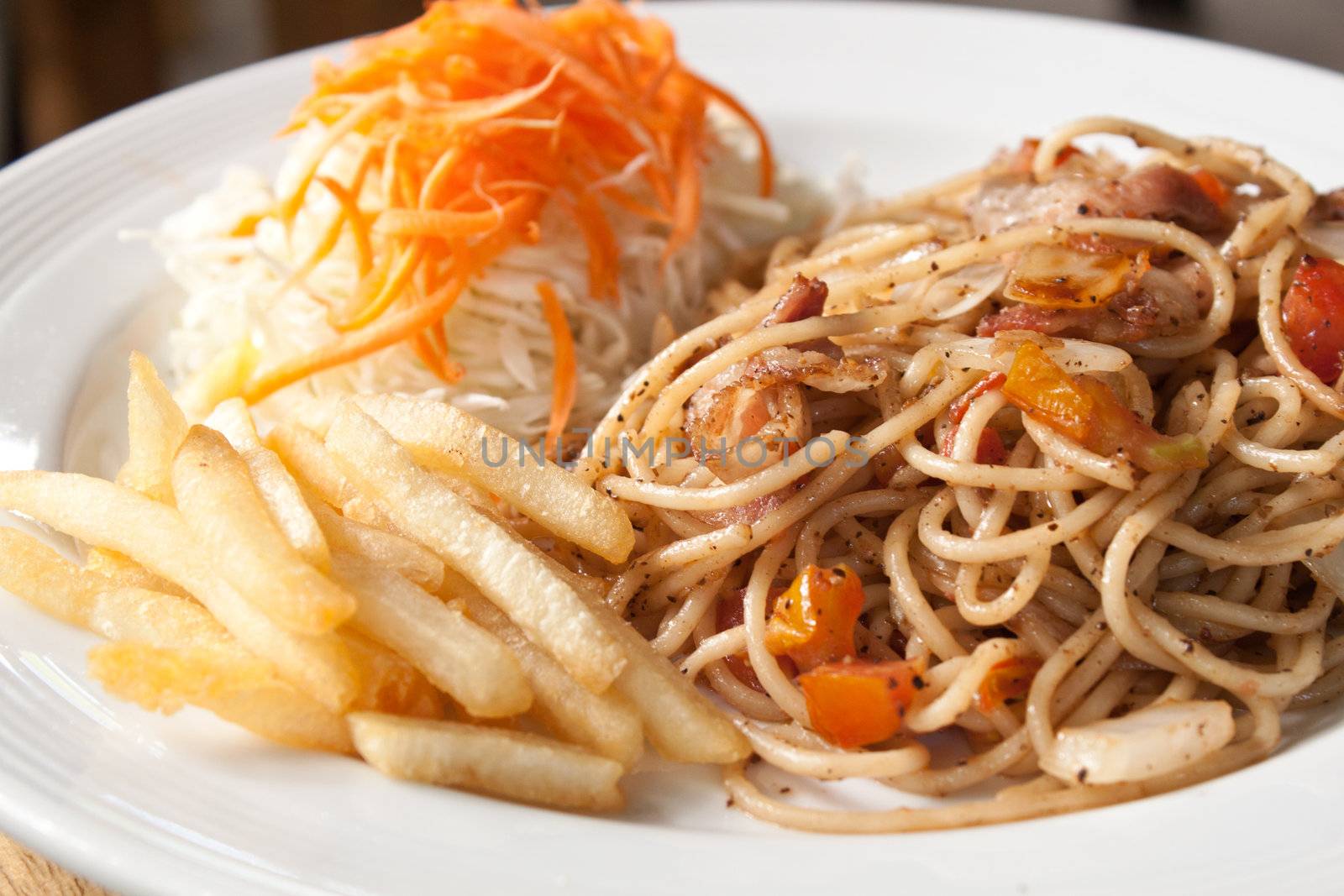 Black pepper and bacon spaghetti in plate with french fries and vegetable salad, shallow depth of field