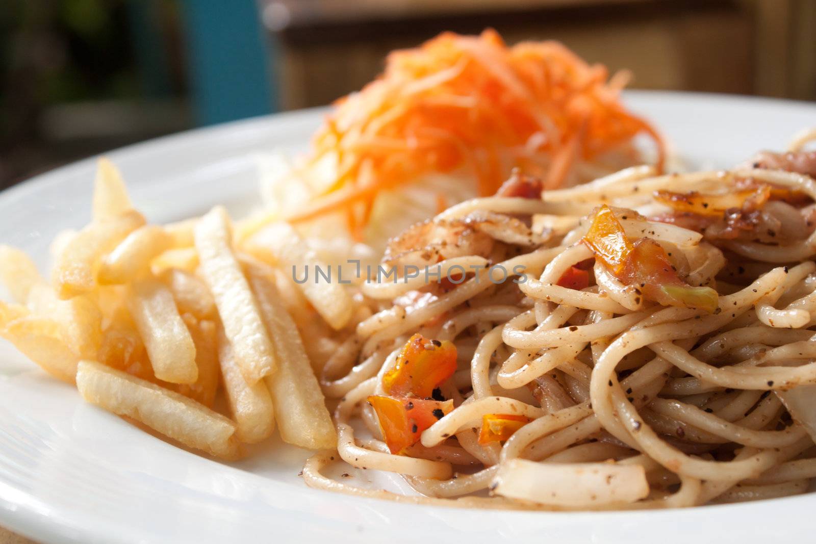 Black pepper and bacon spaghetti in plate with french fries and vegetable salad, shallow depth of field