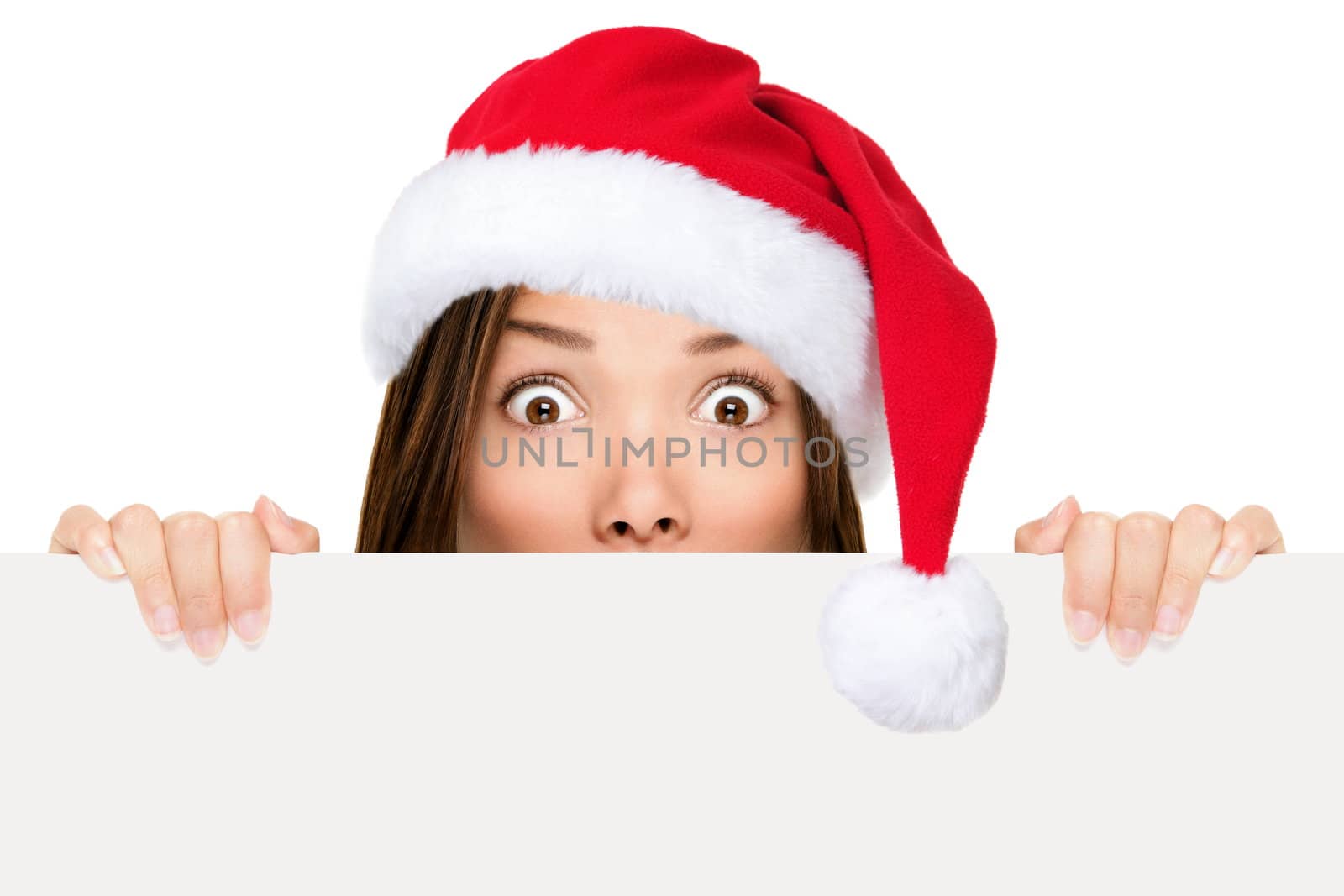 Santa hat woman showing christmas sign peeking over edge wearing red santa hat with funny expression. Mixed race asian chinese / caucasian woman portrait isolated on white background.