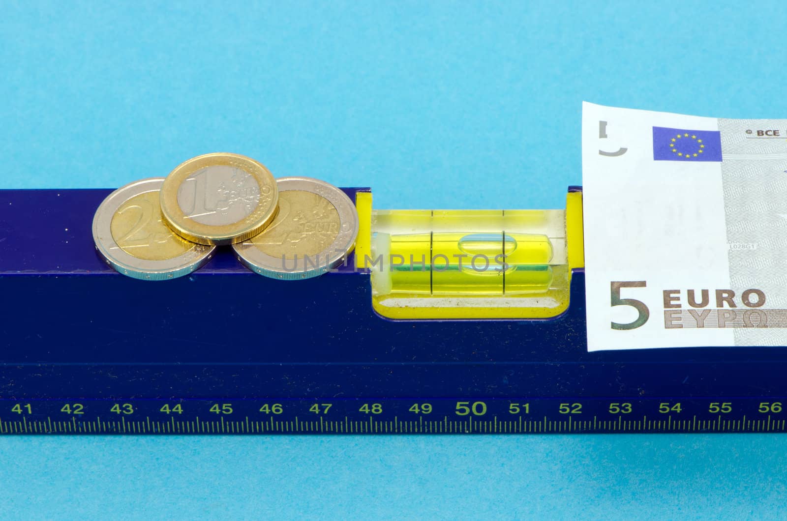 spirit level tool euro banknote and coins on blue background.