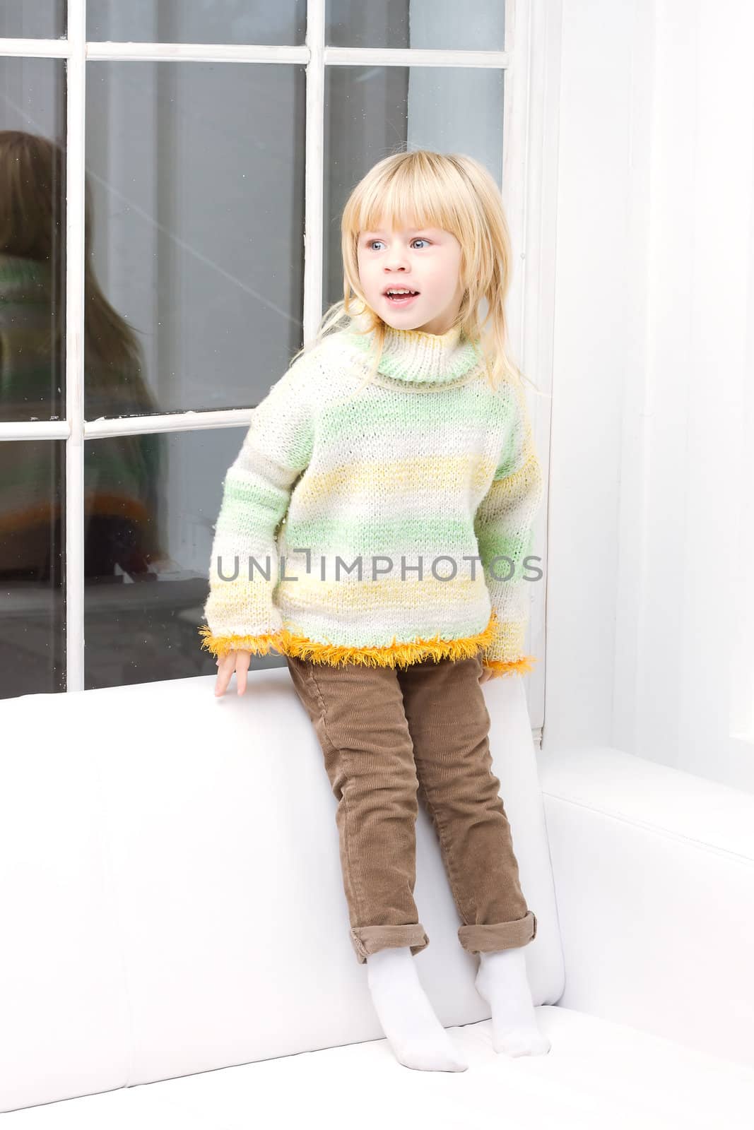 Little girl 3 years old sitting on a white couch near the window