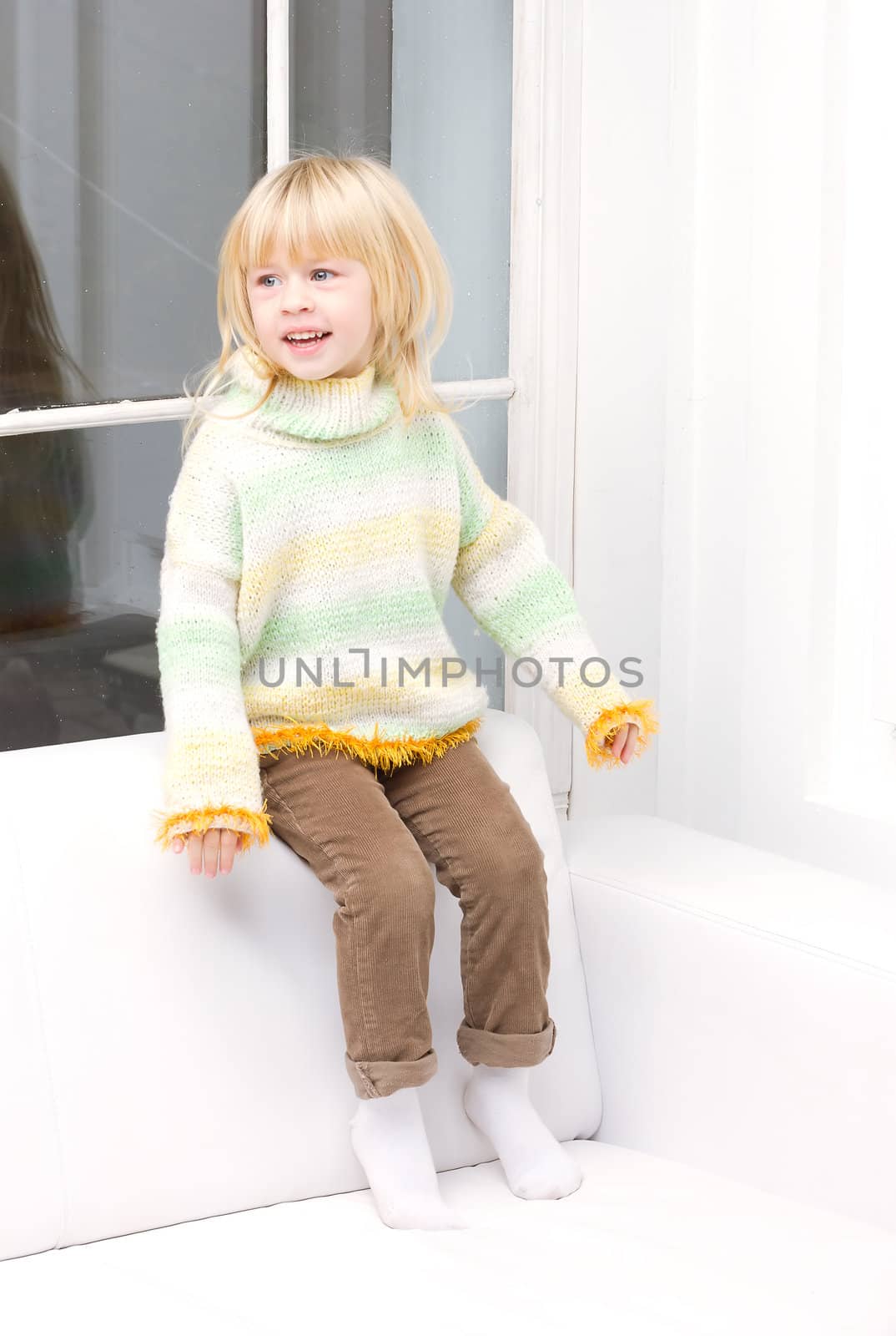 Little girl 3 years old sitting on a white couch near the window