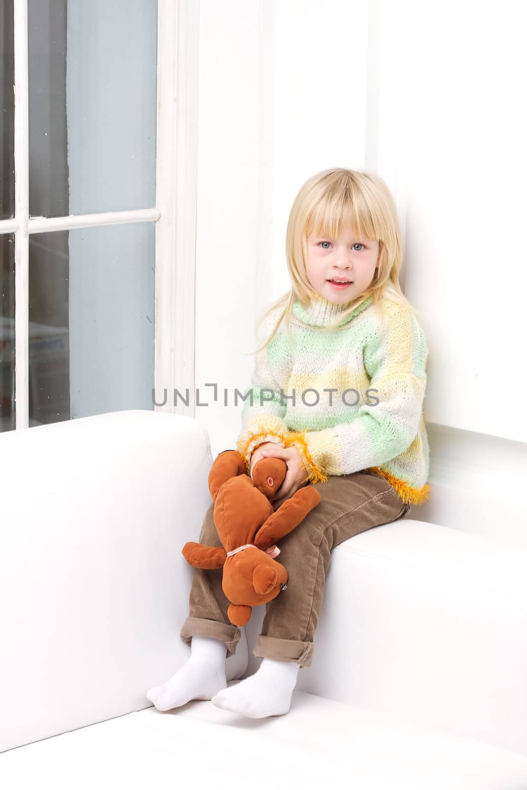 Little Girl 3 years with a brown teddy bear sitting on a white sofa