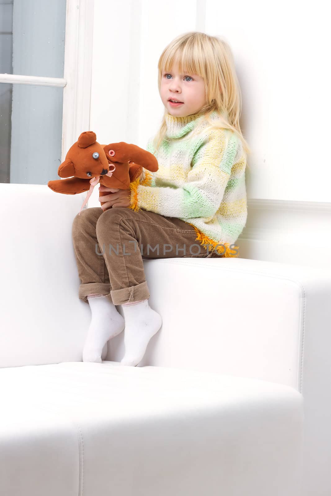 Little Girl 3 years with a brown teddy bear sitting on a white sofa