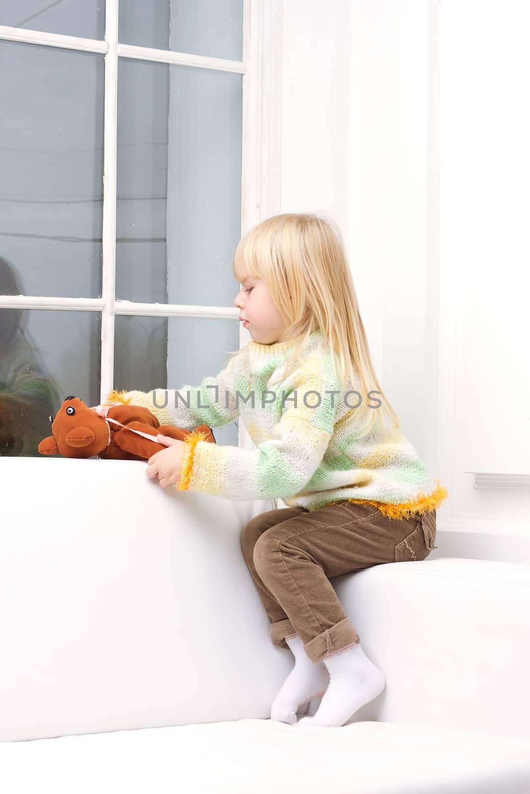 Little Girl 3 years with a brown teddy bear sitting on a white sofa