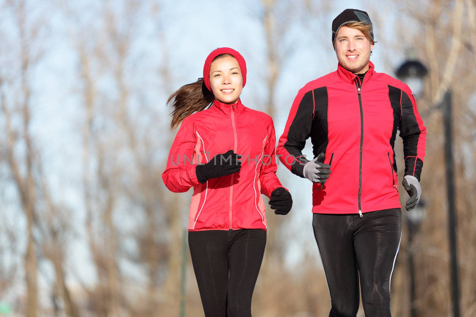 Running. Runners jogging outside. Young couple training outside in warm sport clothing outfit. Beautiful young interracial couple, Asian woman and Cauasian man.