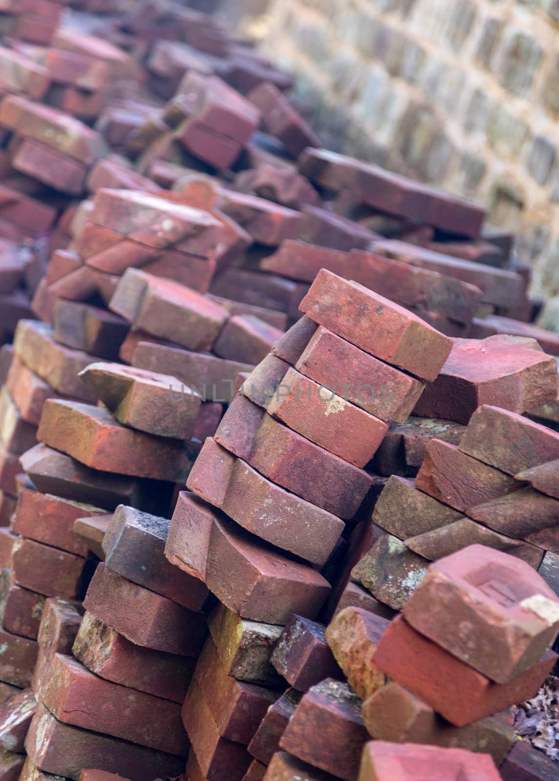 Old hand made bricks in pile stacked against stone wall