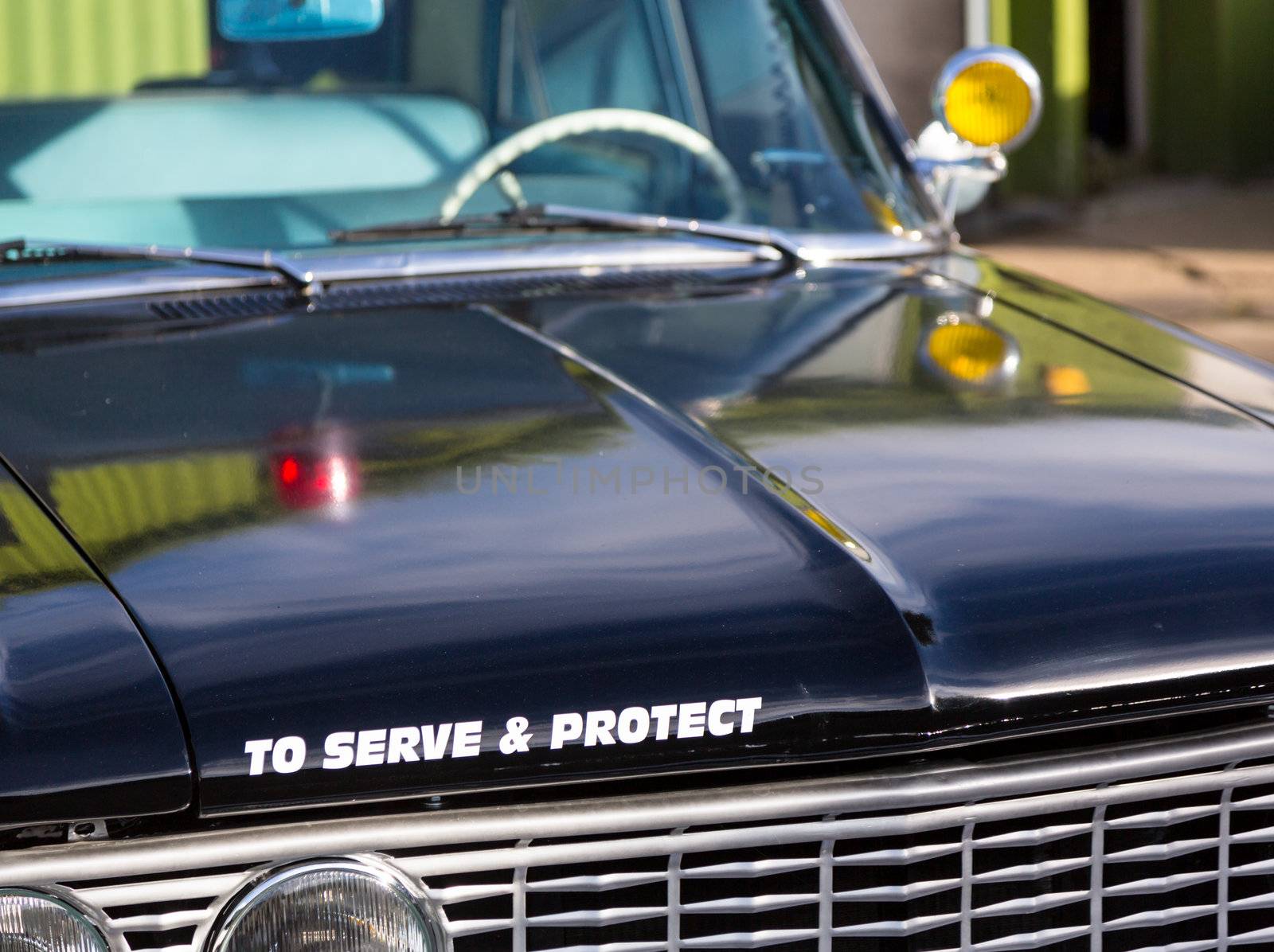 Vintage police car with detail focus on hood and reflections of warning lights in paint