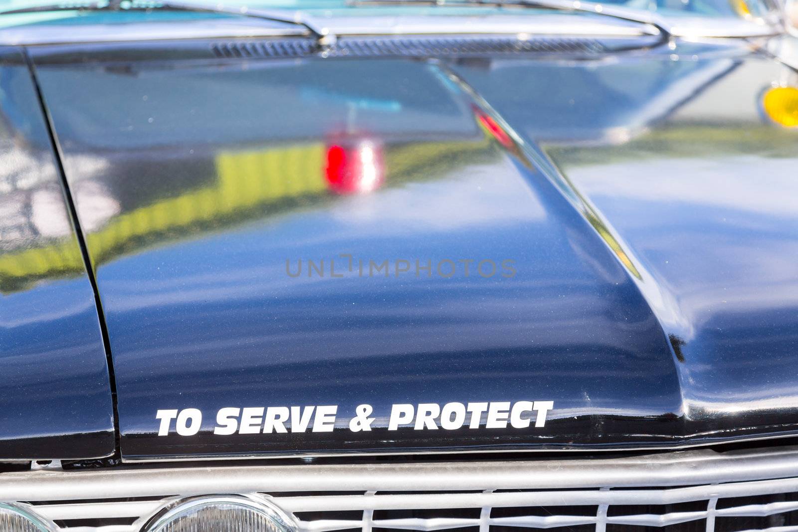 Vintage police car with detail focus on hood and reflections of warning lights in paint