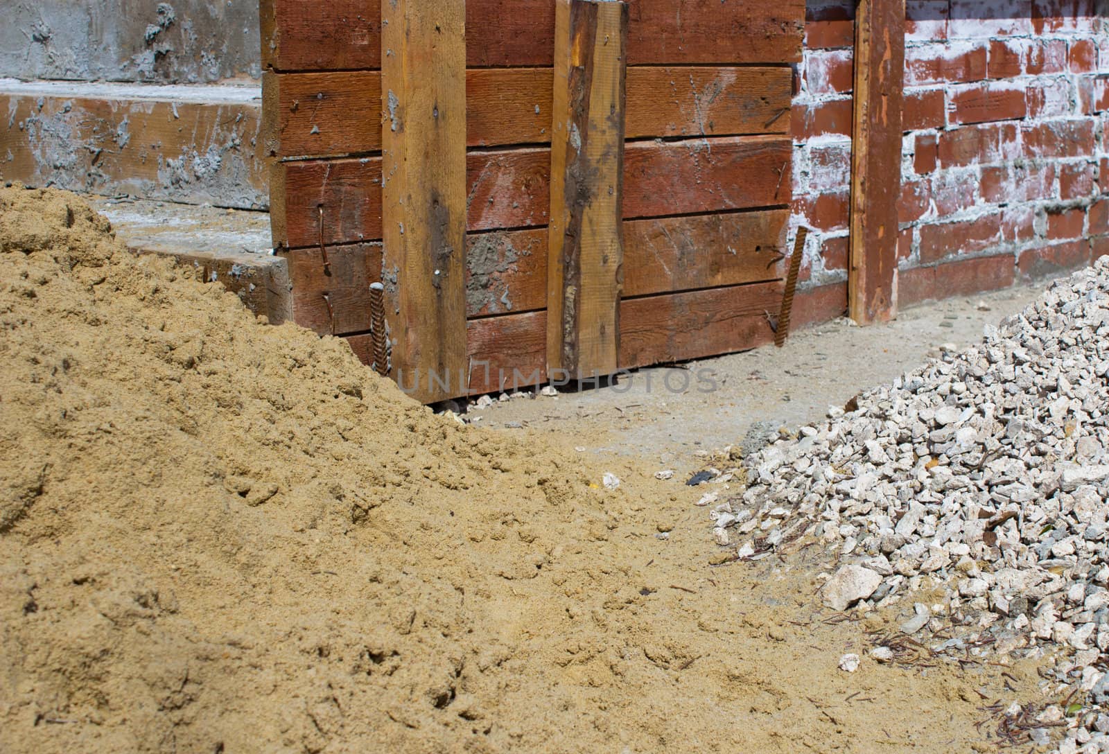 Piles of sand and gravel near a brick wall on a construction site
