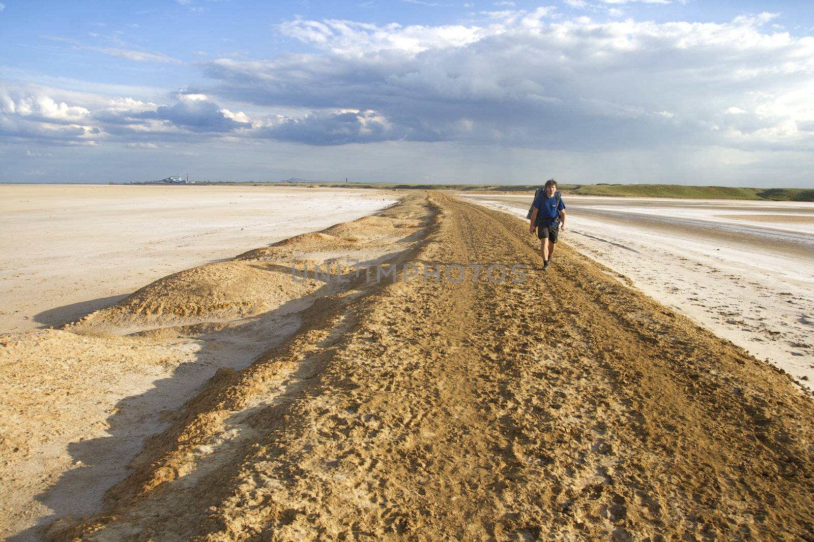 Man with backpack walking among waste landscape, salty lake Baskunckhak in summer