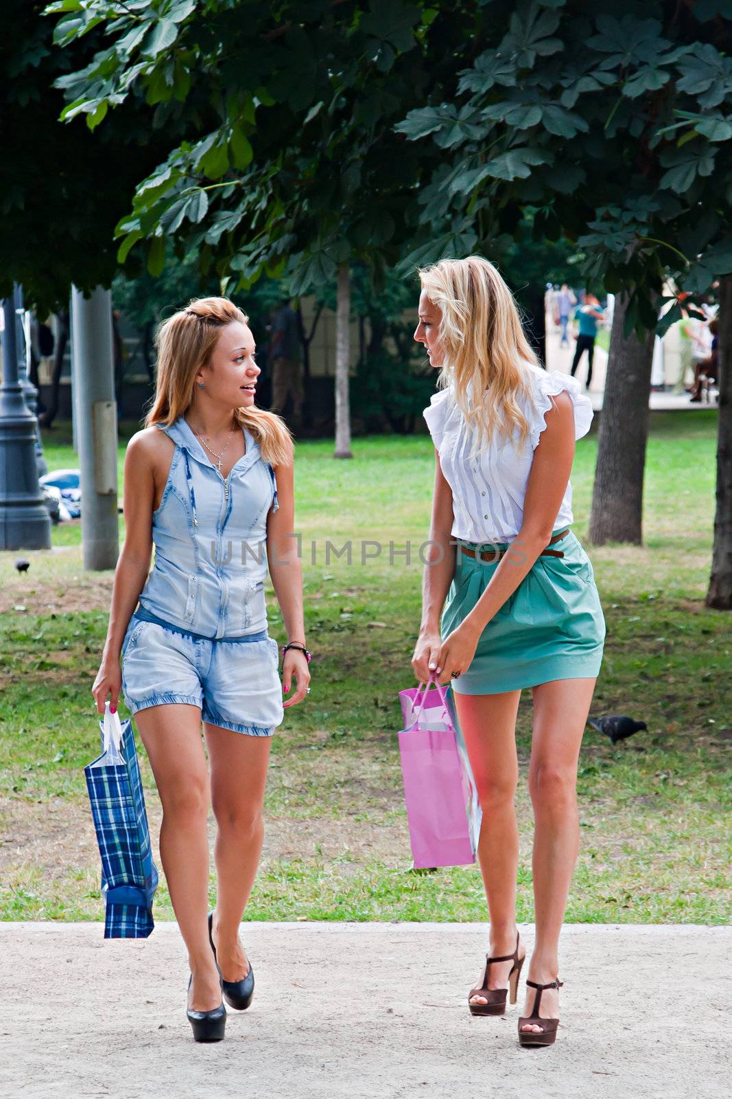 Two beautiful and young girl walking in the park after shopping in a store