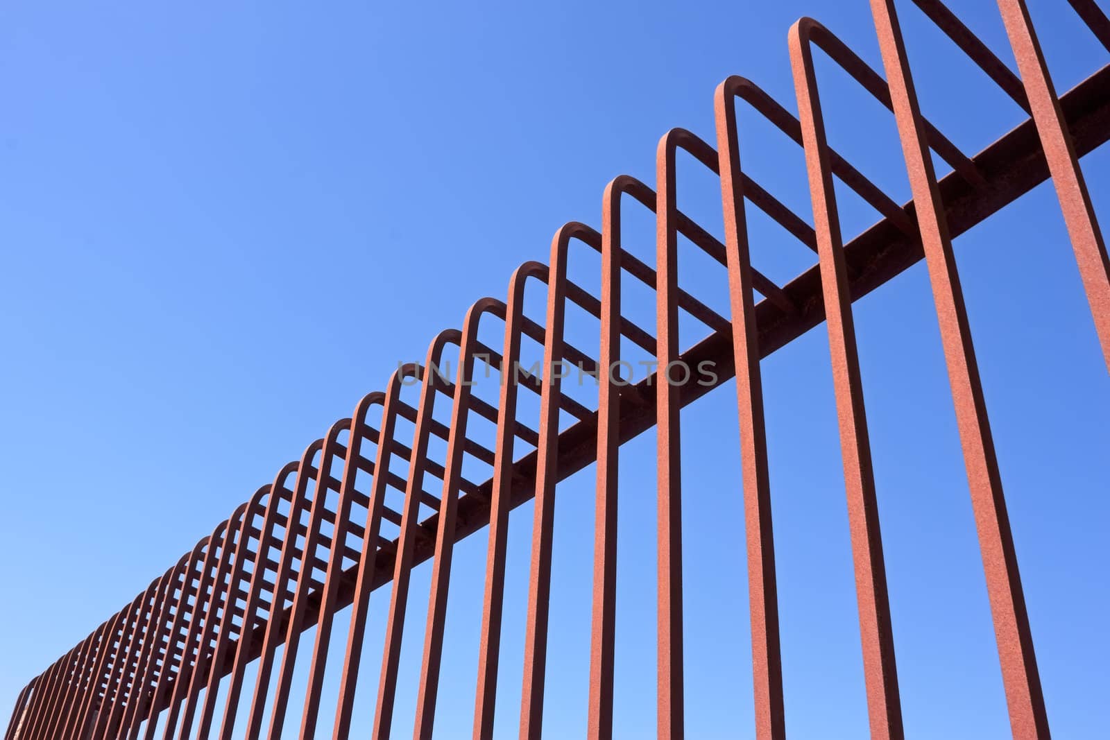 Fragment of fence with bent metal rods against a blue sky