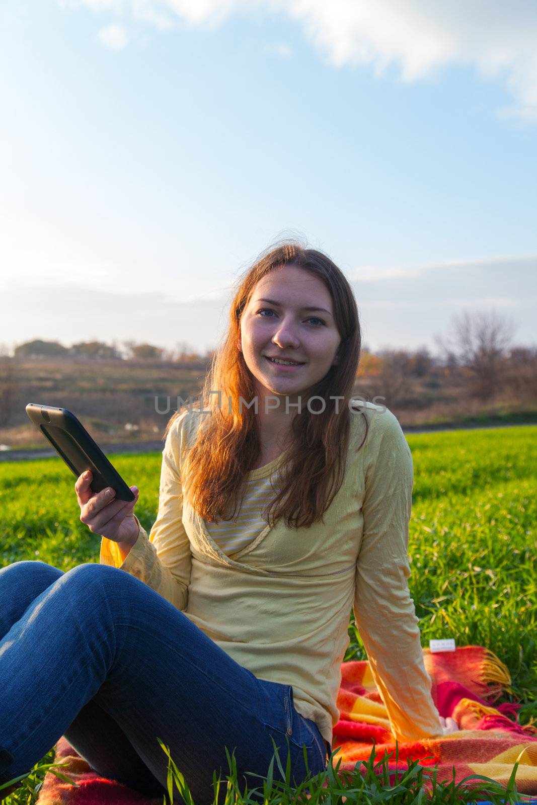 Teen girl reading electronic book sitting outdoors