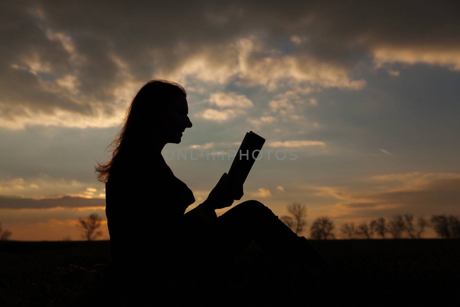 Teen girl reading book outdoors by AndreyKr