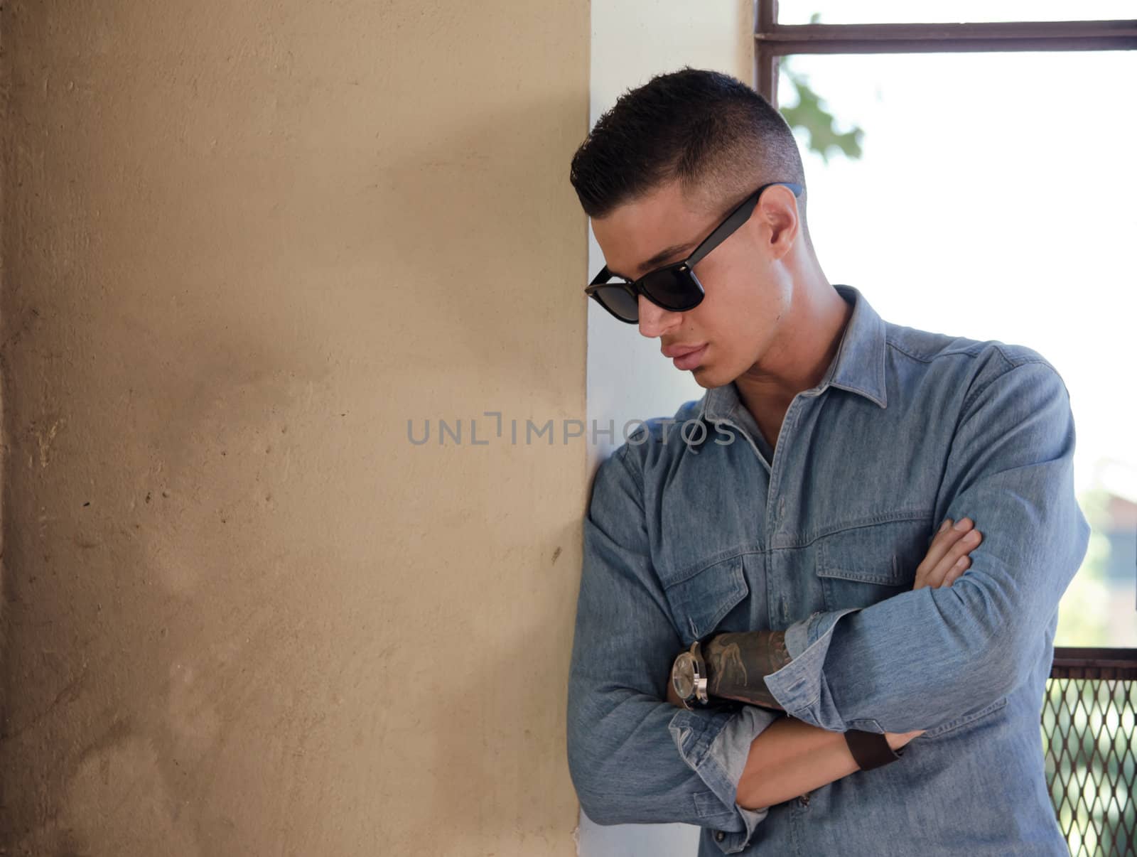 Good looking male model with sunglasses looking down, with large copy-space