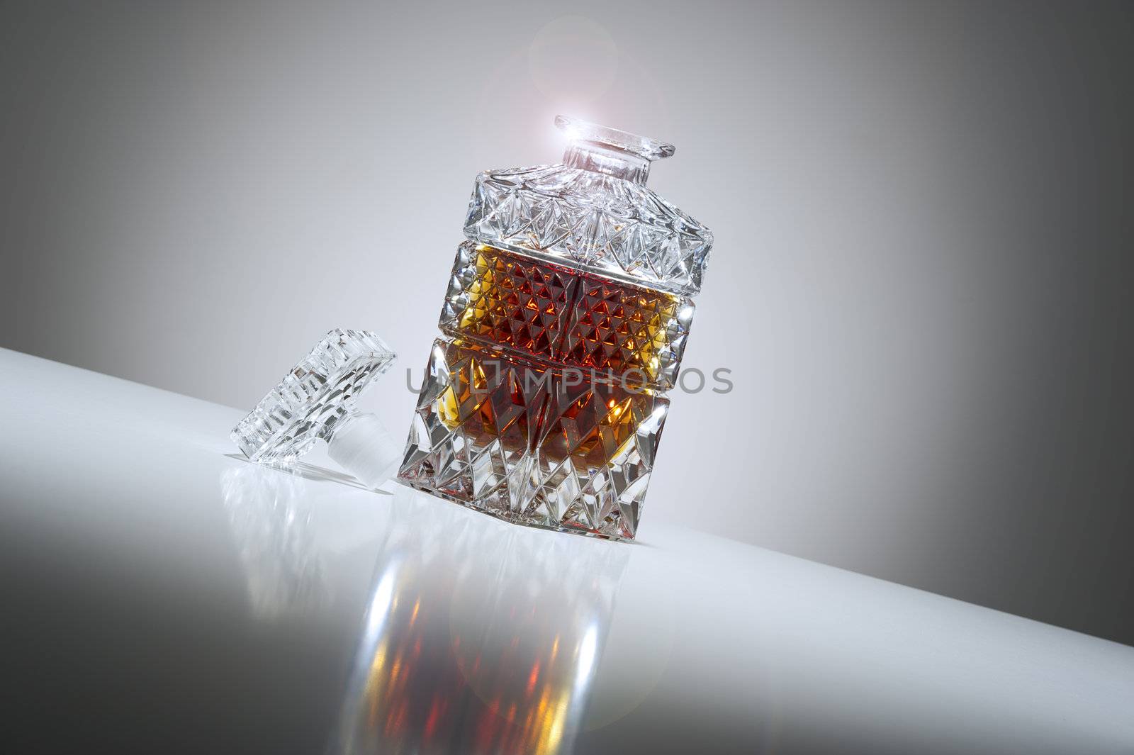 Tilted low angle view of an open elegant crystal whiskey or brandy decanter with a sparkling rim and a graduated grey background with a highlight and reflection
