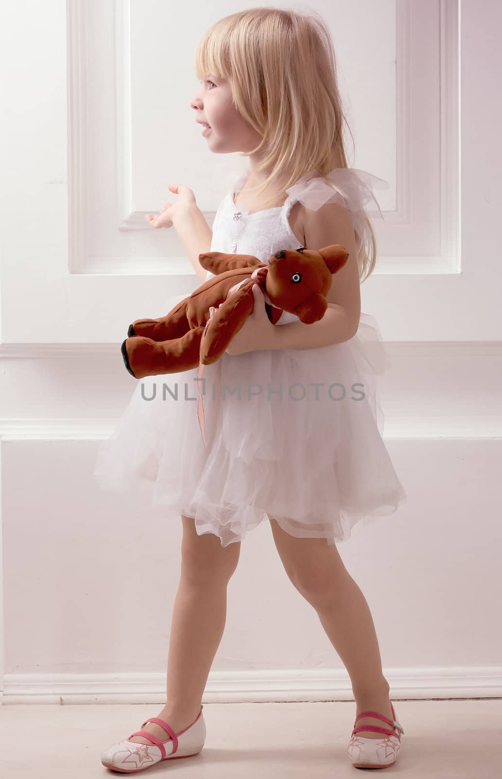 3 years old girl in a white dress with a toy against the wall