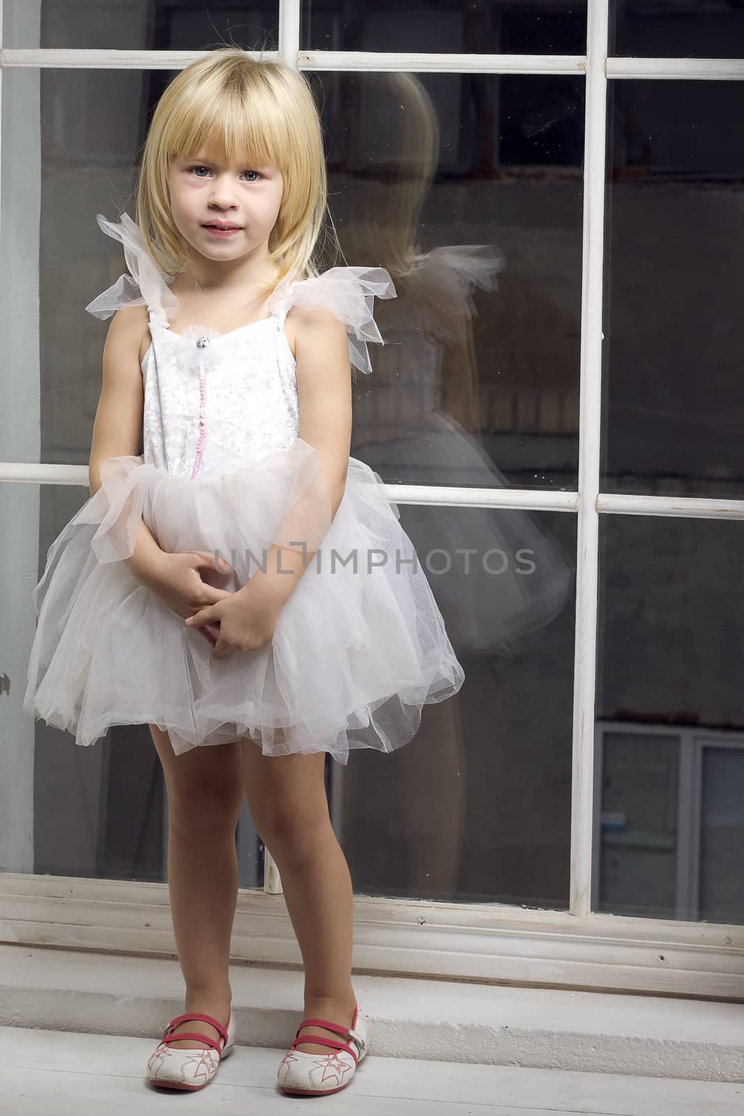 Girl 3 years old in a beautiful white dress near the winter window