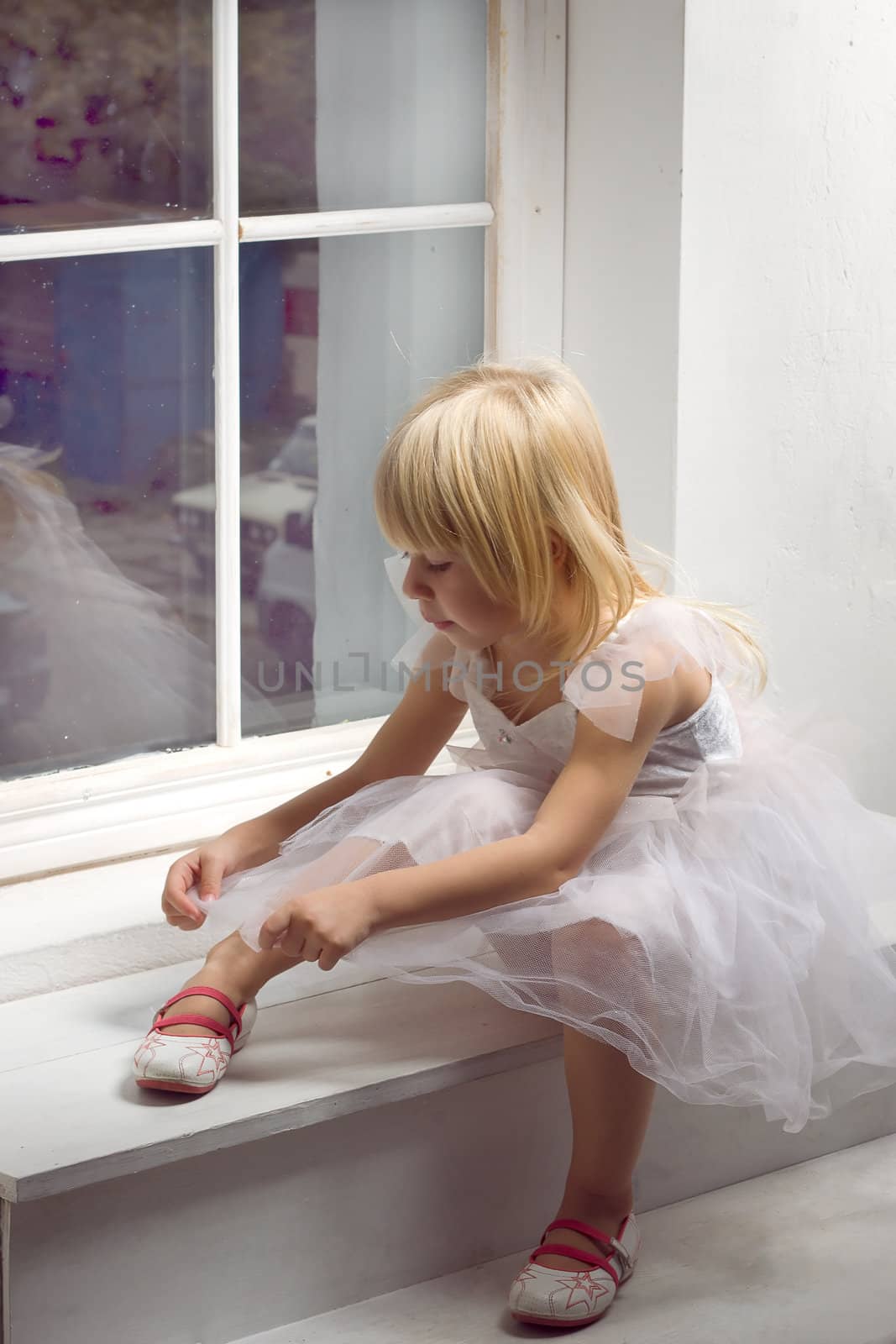 Girl 3 years old in a beautiful white dress near the winter window