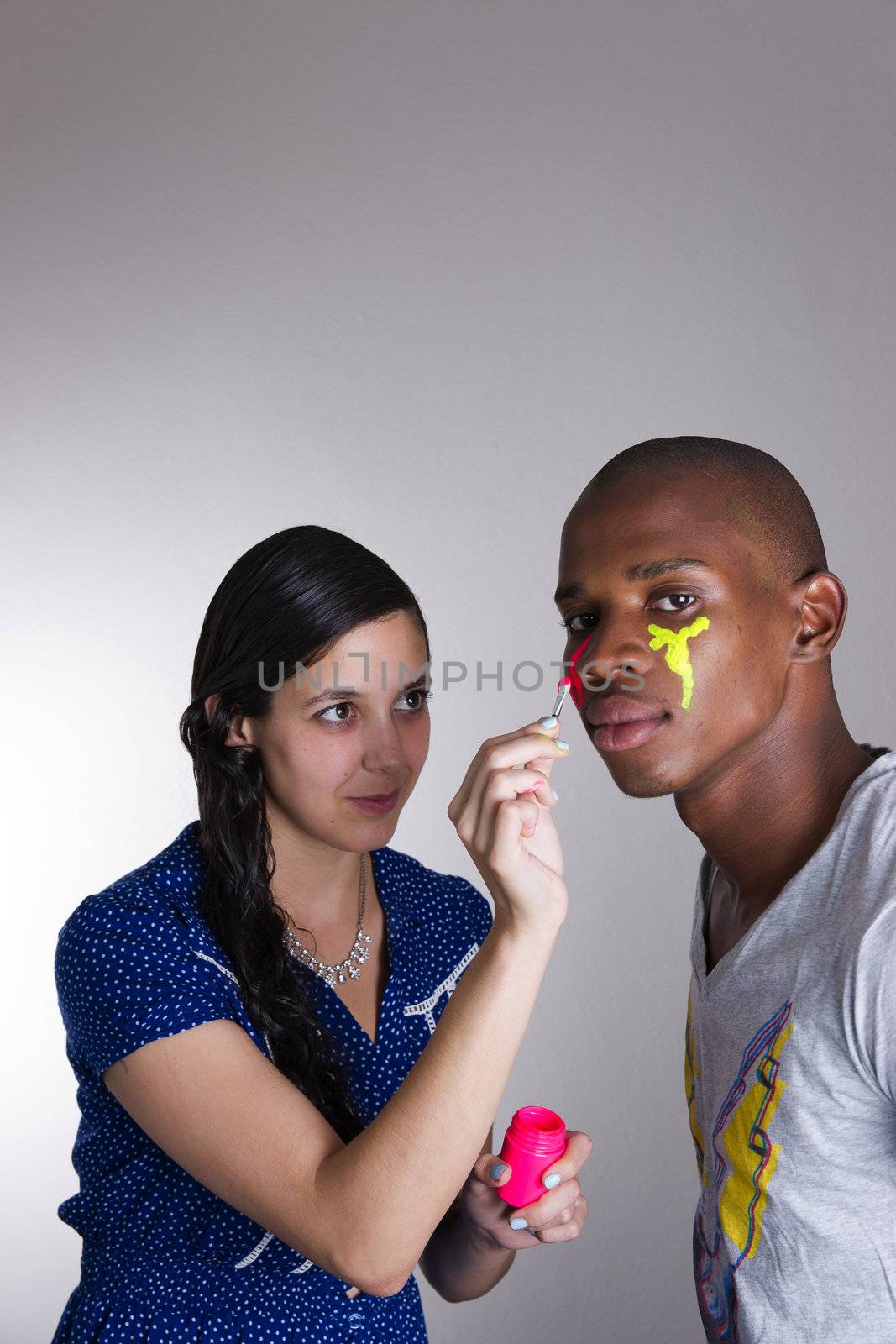 Young couple in studio painting with colors on their faces by jjgerber