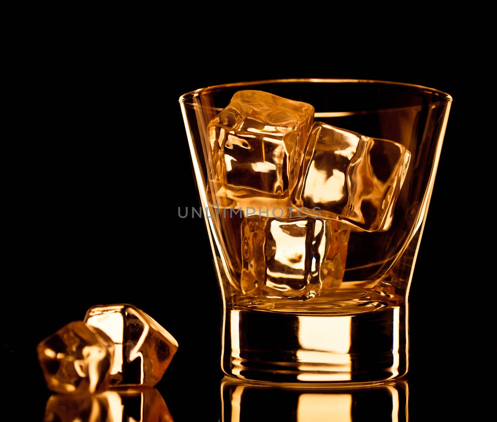 Empty whiskey glass with ice cubes on black background