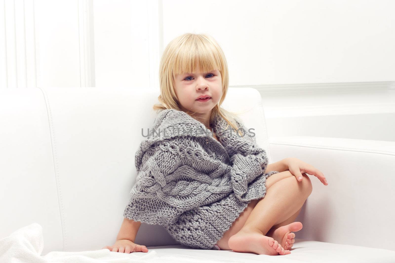 Girl 3 years old in a gray knit sweater sitting on a sofa