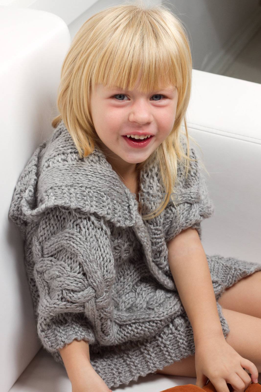 Girl 3 years old in a gray knit sweater sitting on a sofa