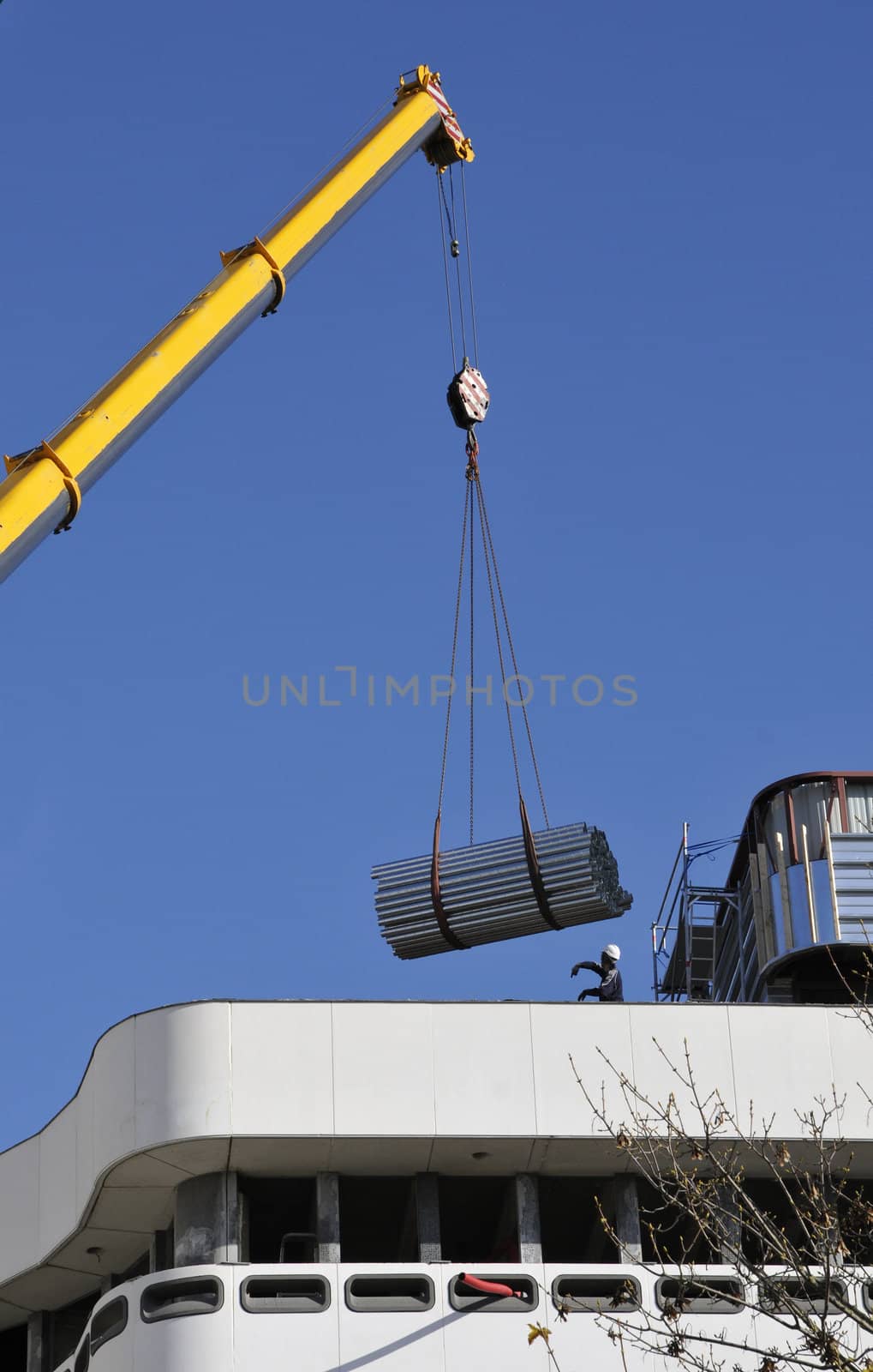 Yellow Crane carrying some metallic tubes with a man to help