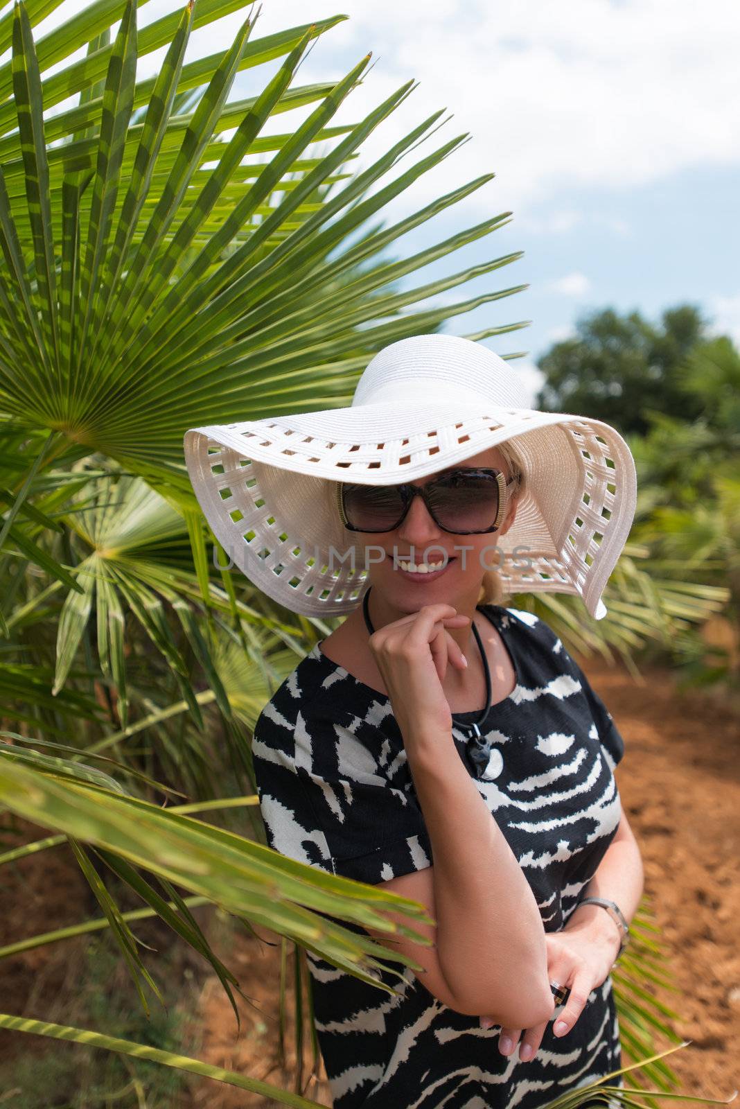 Blond woman at tropical travel resort  in white hat smiling.