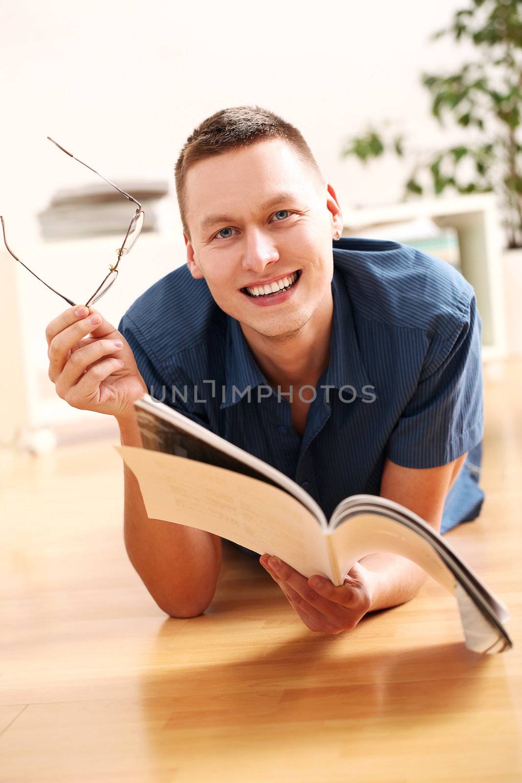 Lying young man with glasses reading magazine at home