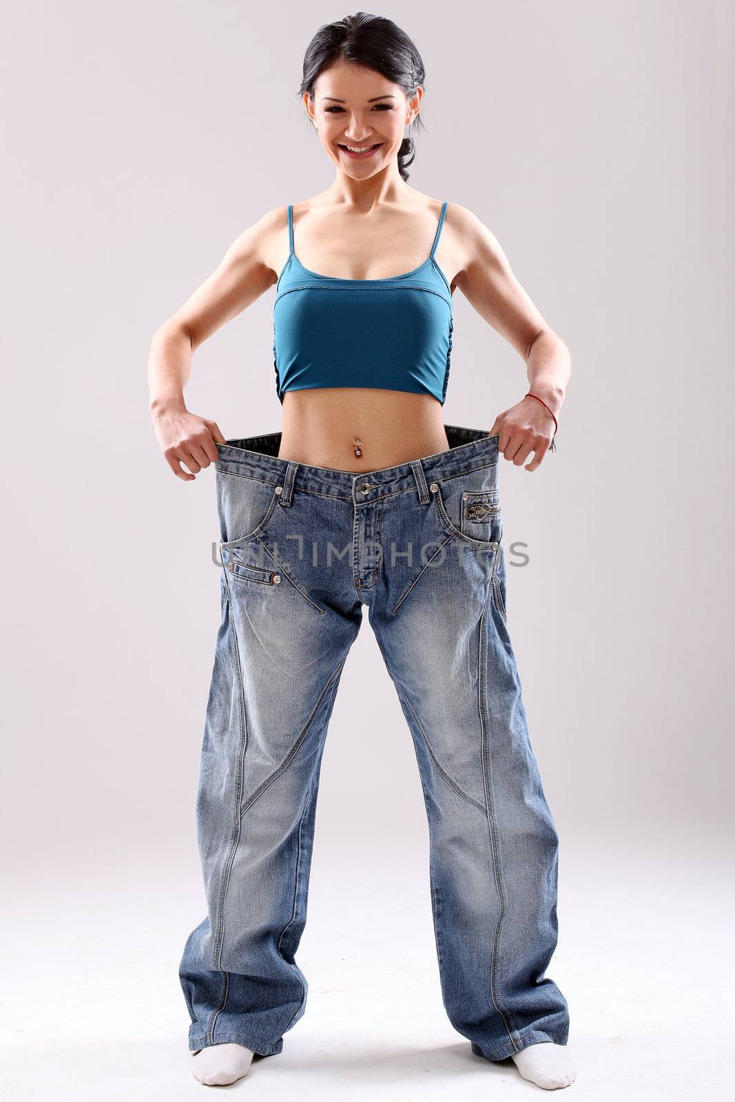 Cute slim girl wearing old jeans after weight loss, in studio