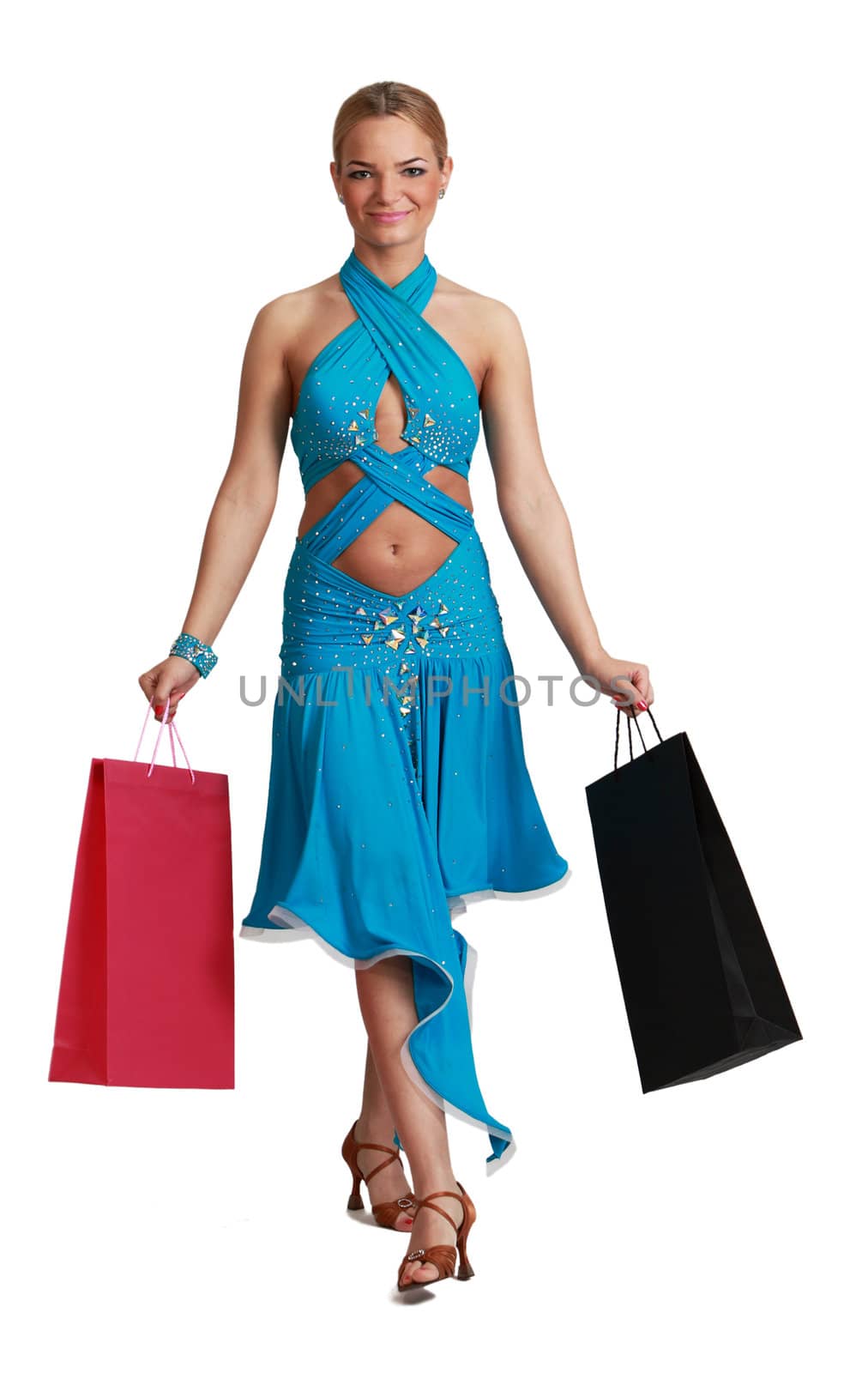 Young blonde woman in a fancy dress with shopping bags walking to the camera against a white background.