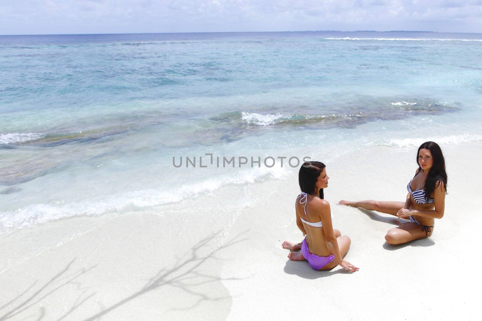 Two beautiful women sitting on beach and talking