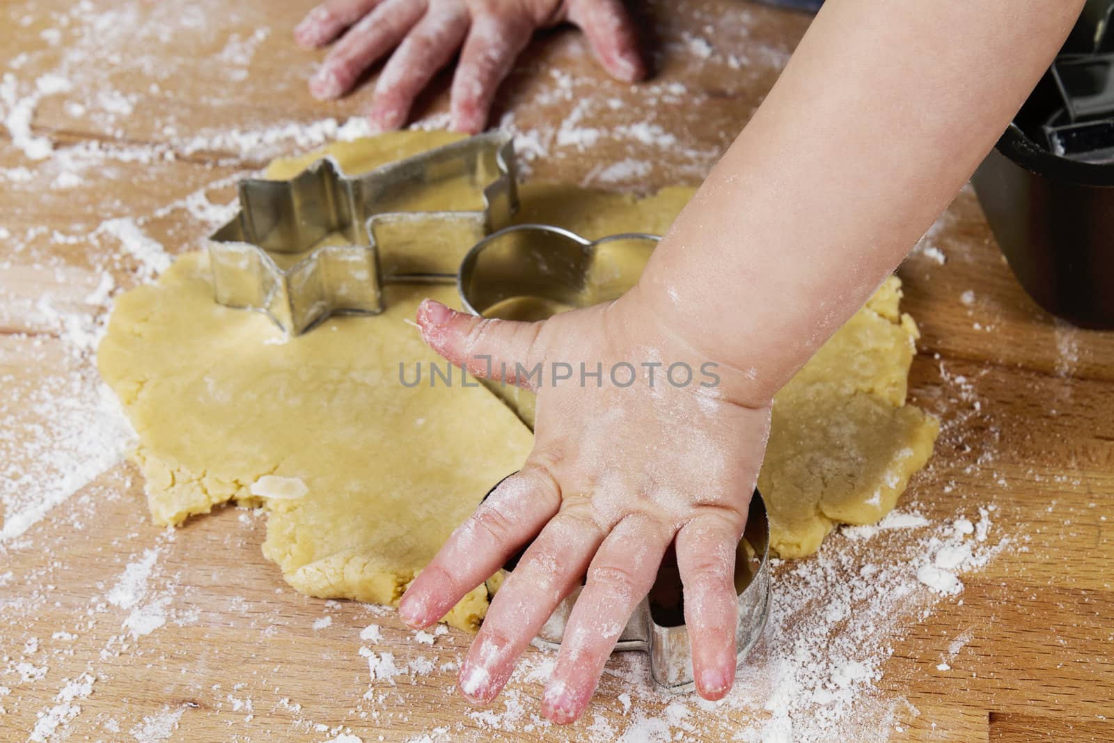 small childrens hands with dough on wooden table with flour
