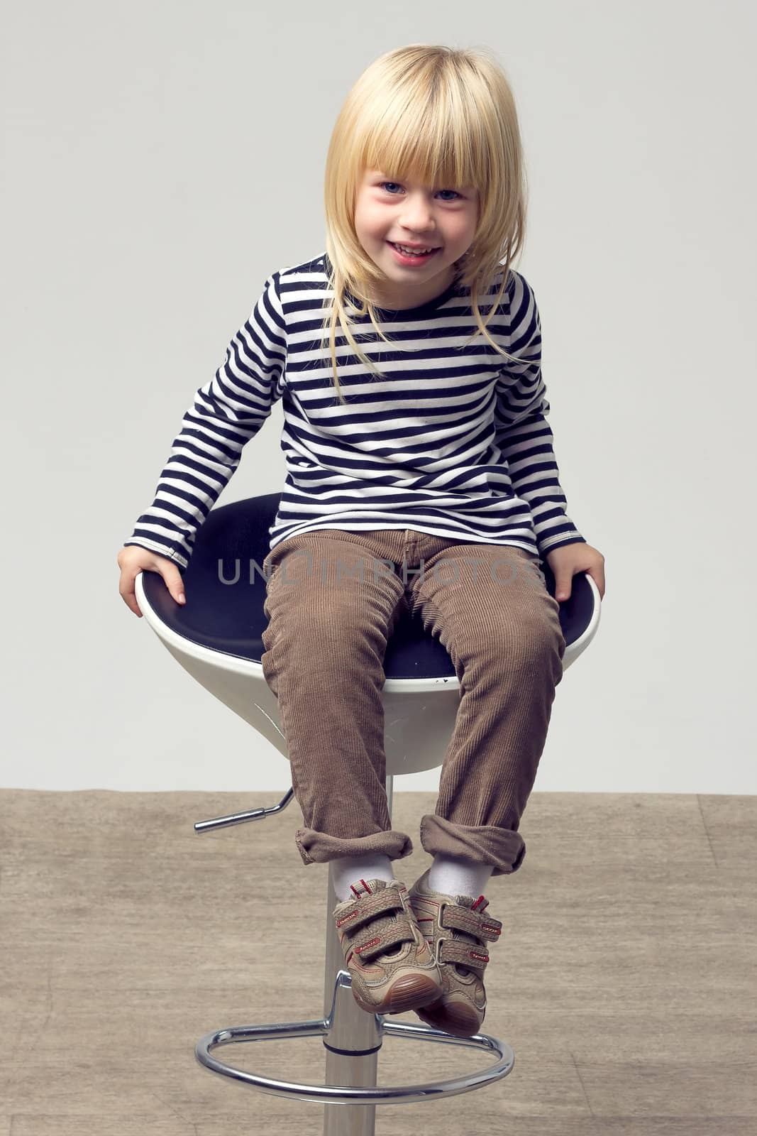 Blonde girl 3 years old in jeans sits on a high chair