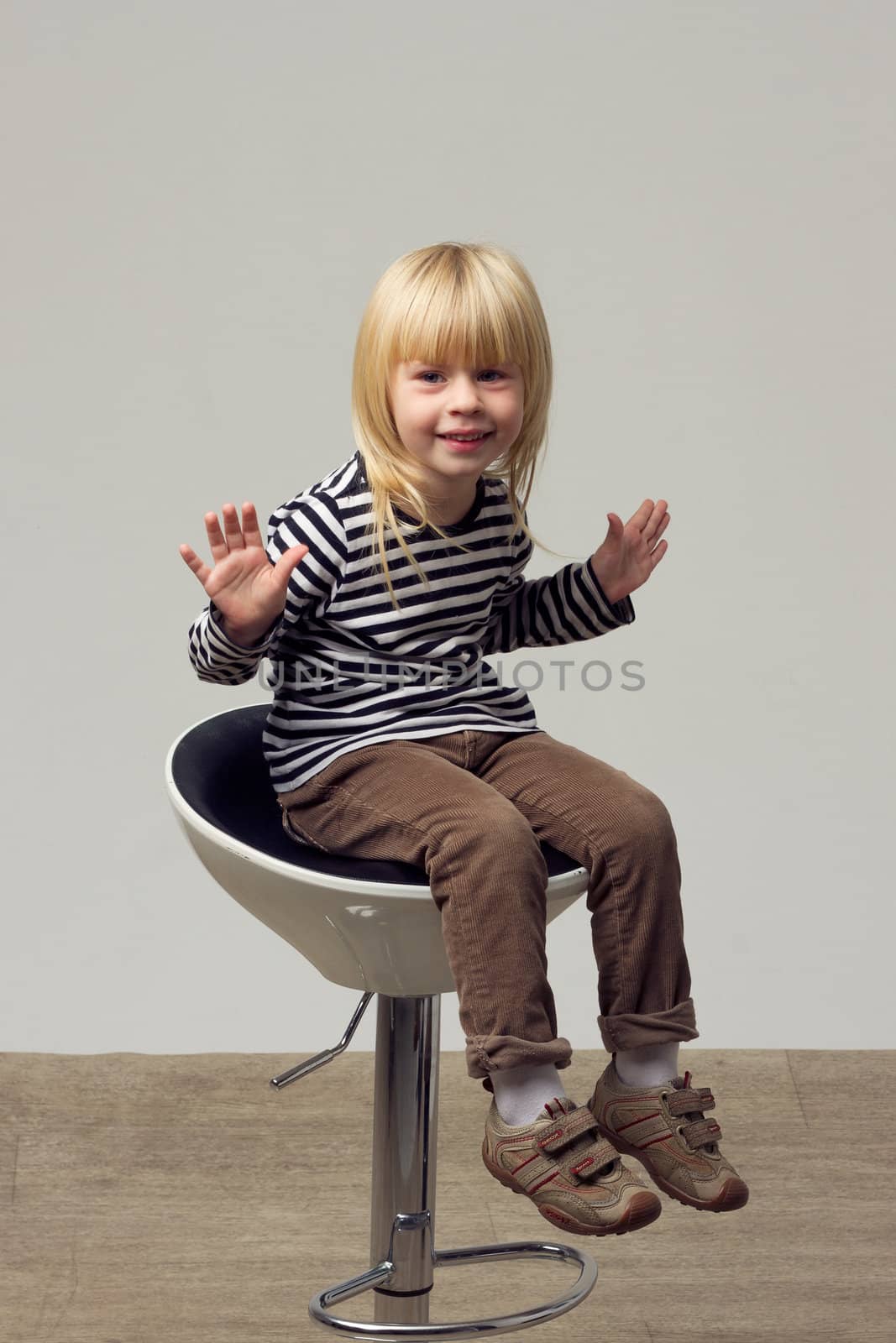 Blonde girl 3 years old in jeans sits on a high chair