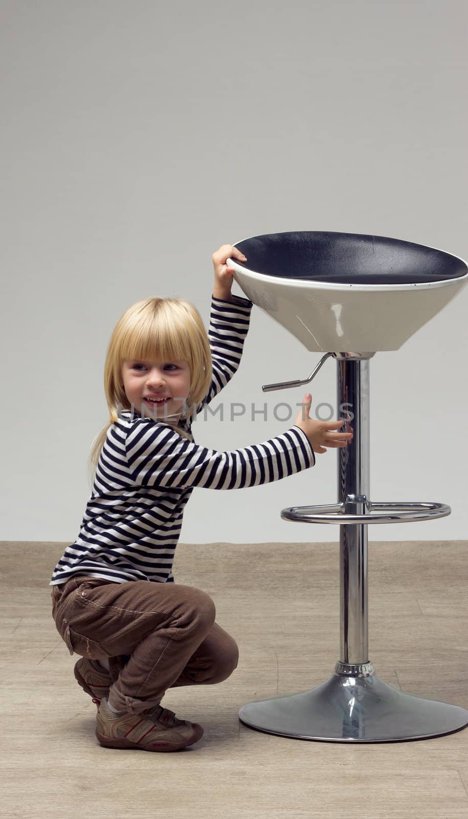 Blonde girl 3 years sat near a high chair and doing something
