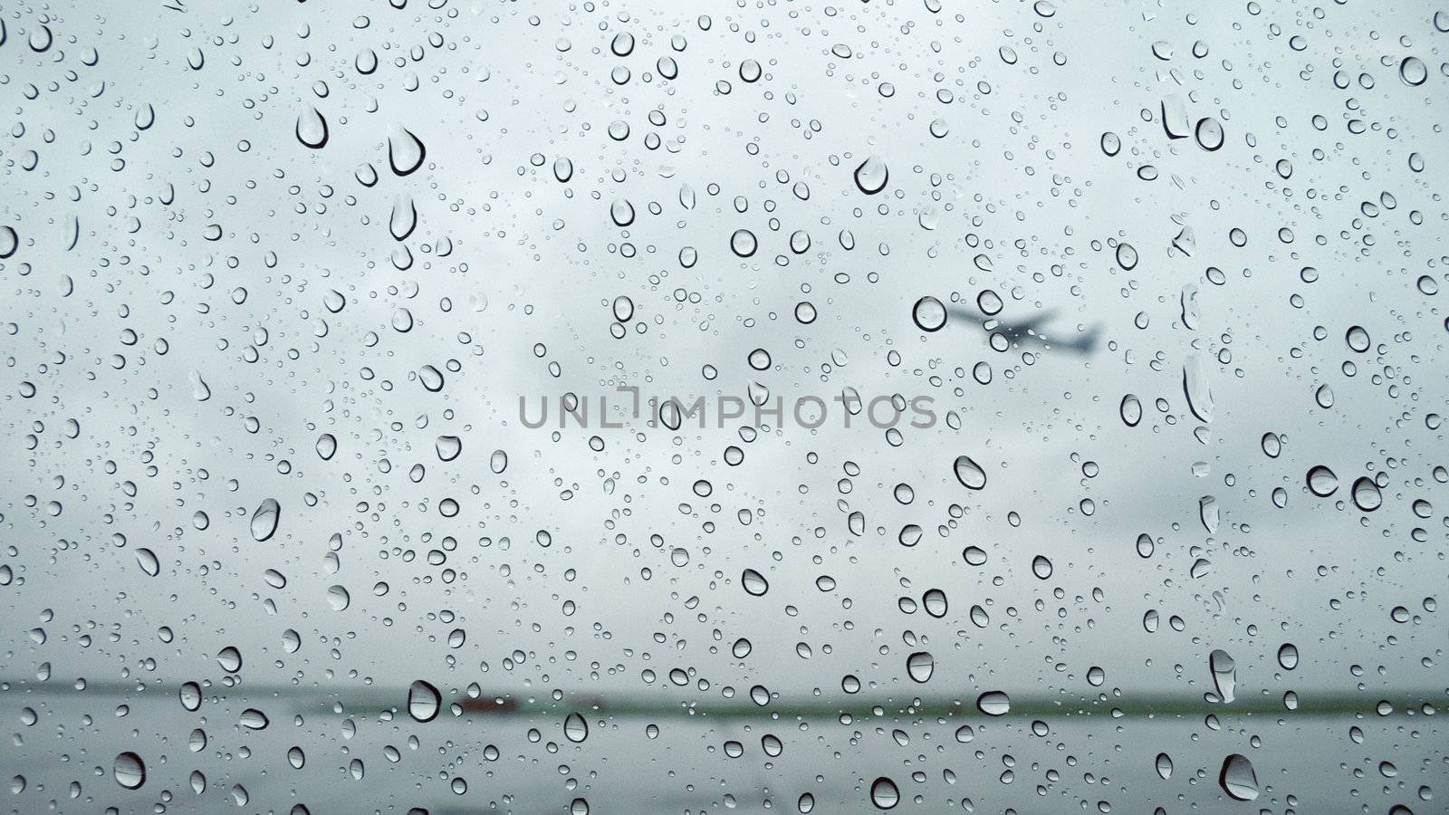 raindrops background on airport window with flying plane behind
