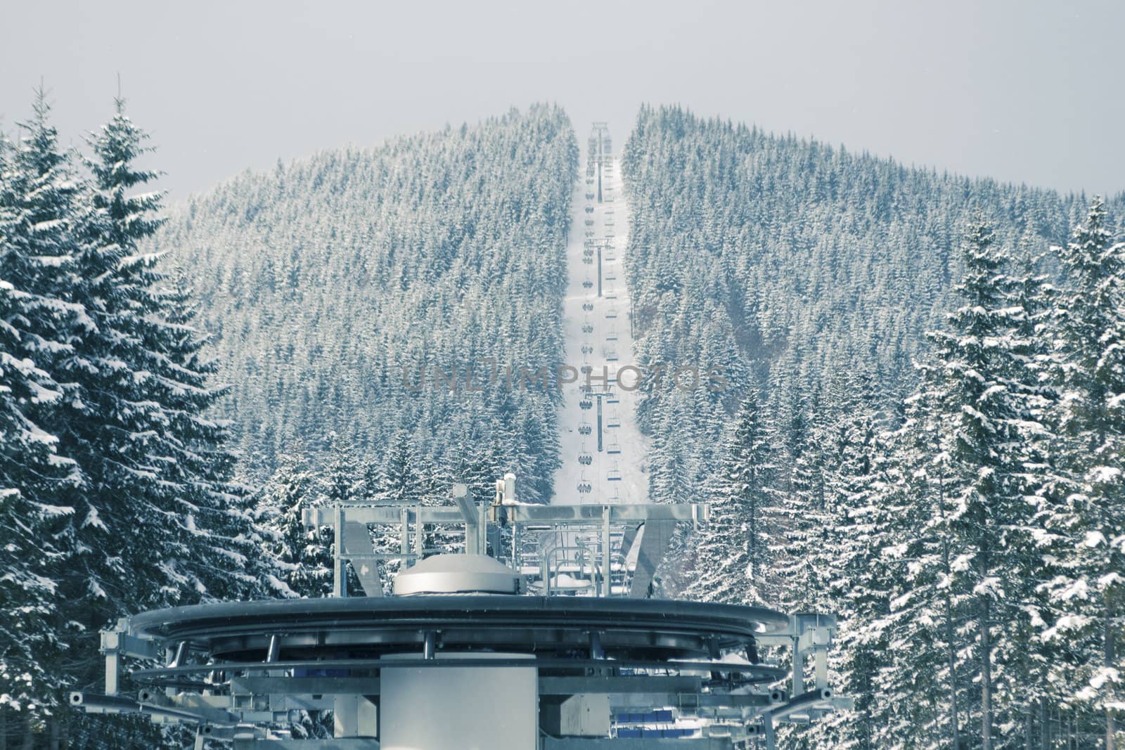 ski lift wheel with mountain and  moving sportsmans; focus on foreground wheel and forest 