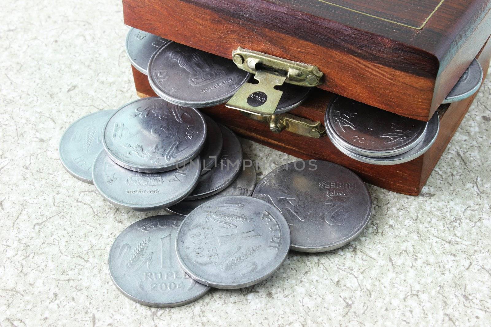 Indian currency coins overflowing from a wooden chest