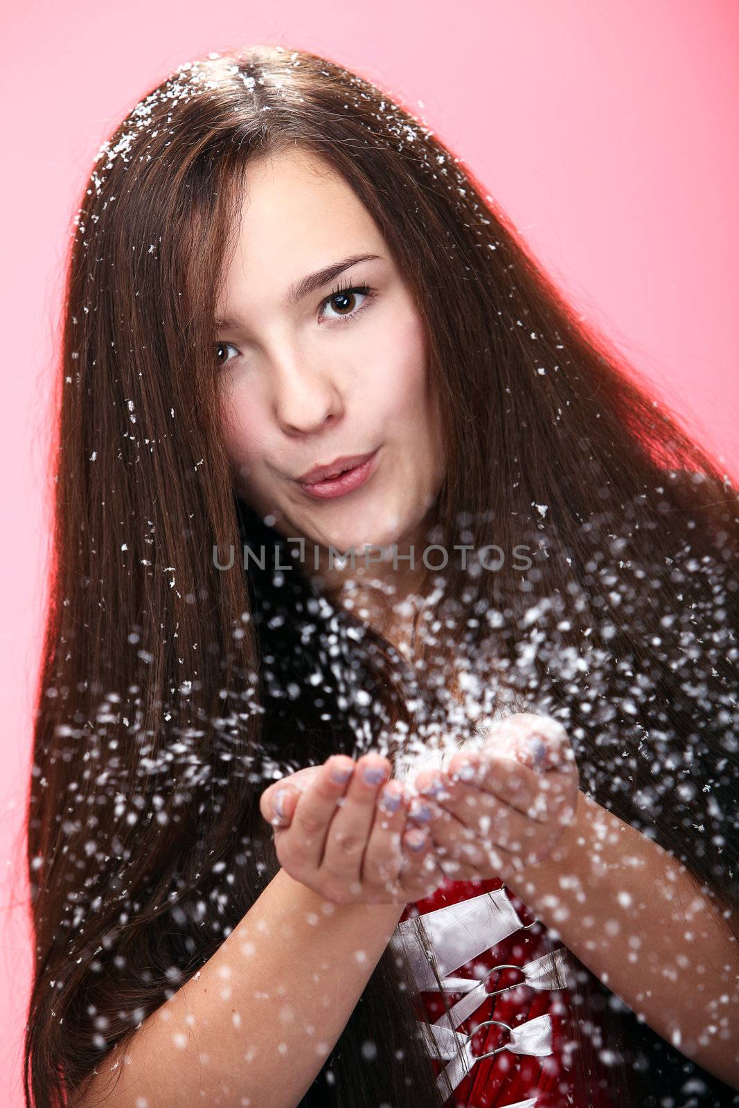 Beautiful and attractive girl blowing on christmas snow isolated on a red