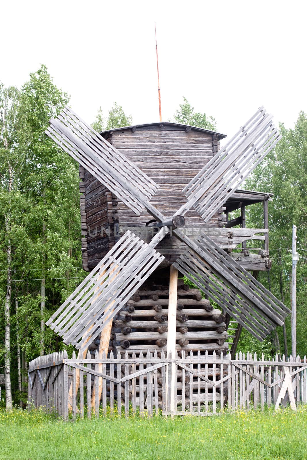 A traditional wooden russian windmill in front of a forest
