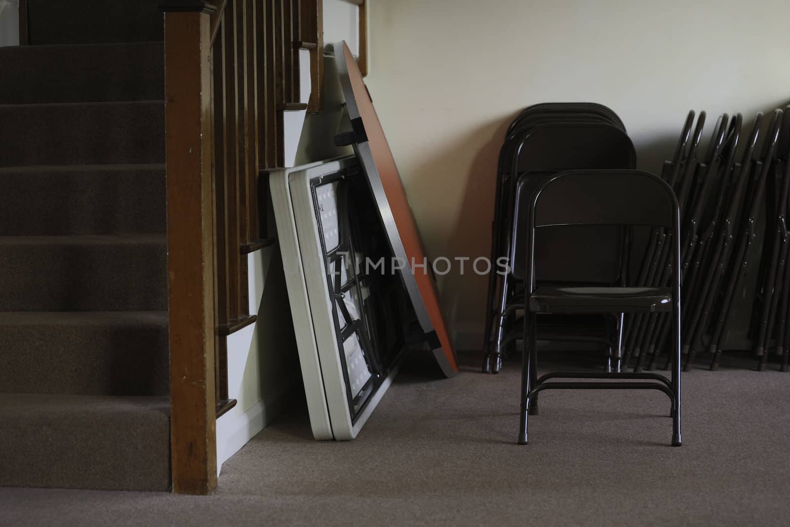 Folding tables and chairs stacked at the bottom of a stairwell in an entertainment venue, meeting hall or school