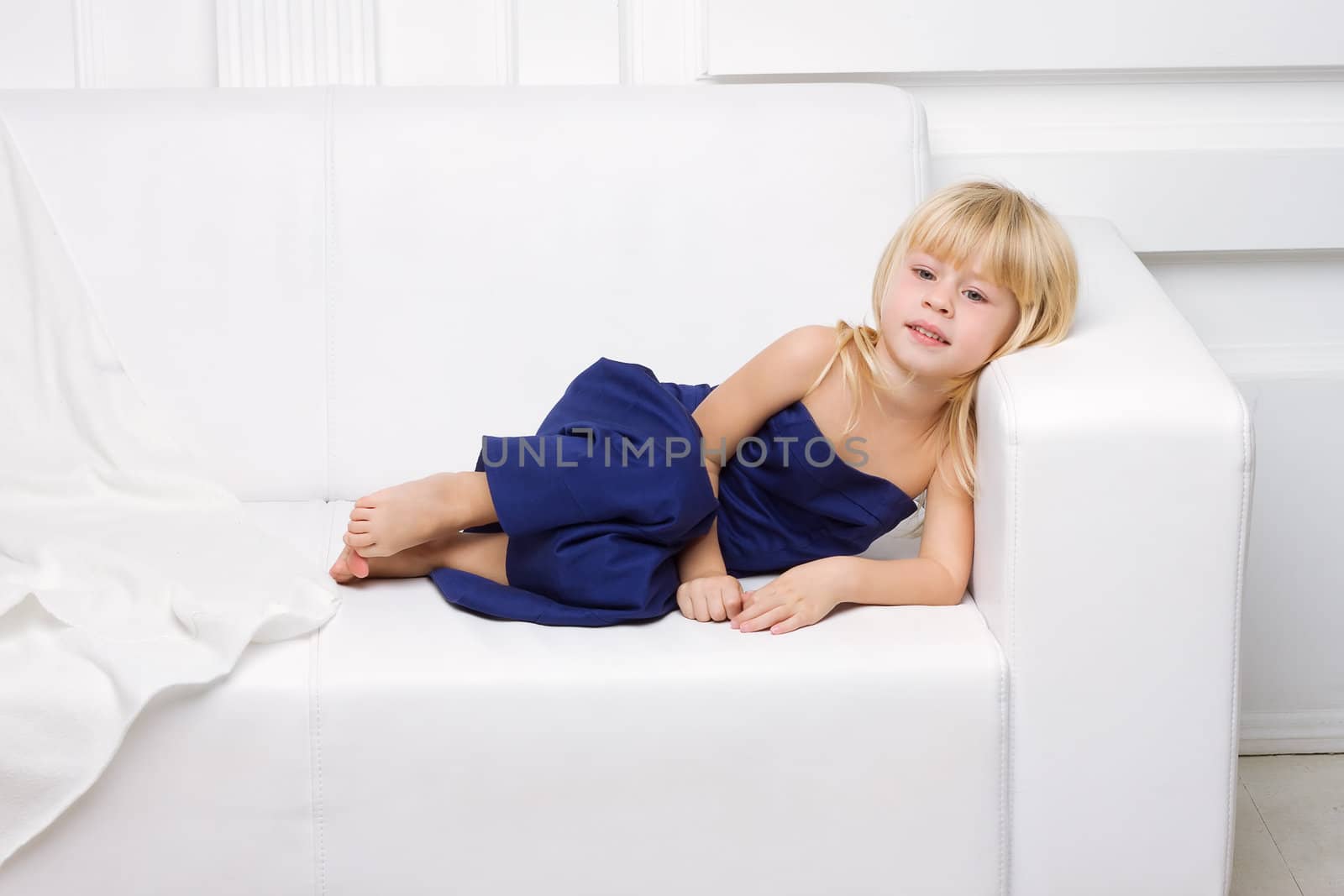 3 years old girl is in a blue dress on a white sofa