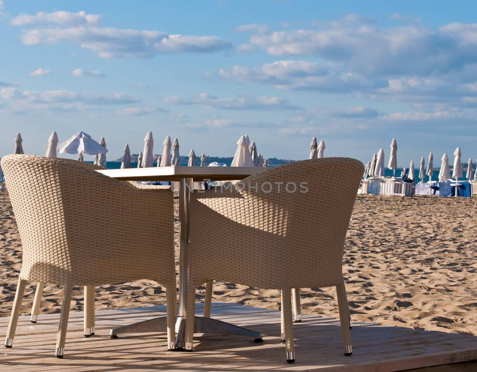 View of the beach with street cafe , table, chair , loungers and umbrellas.