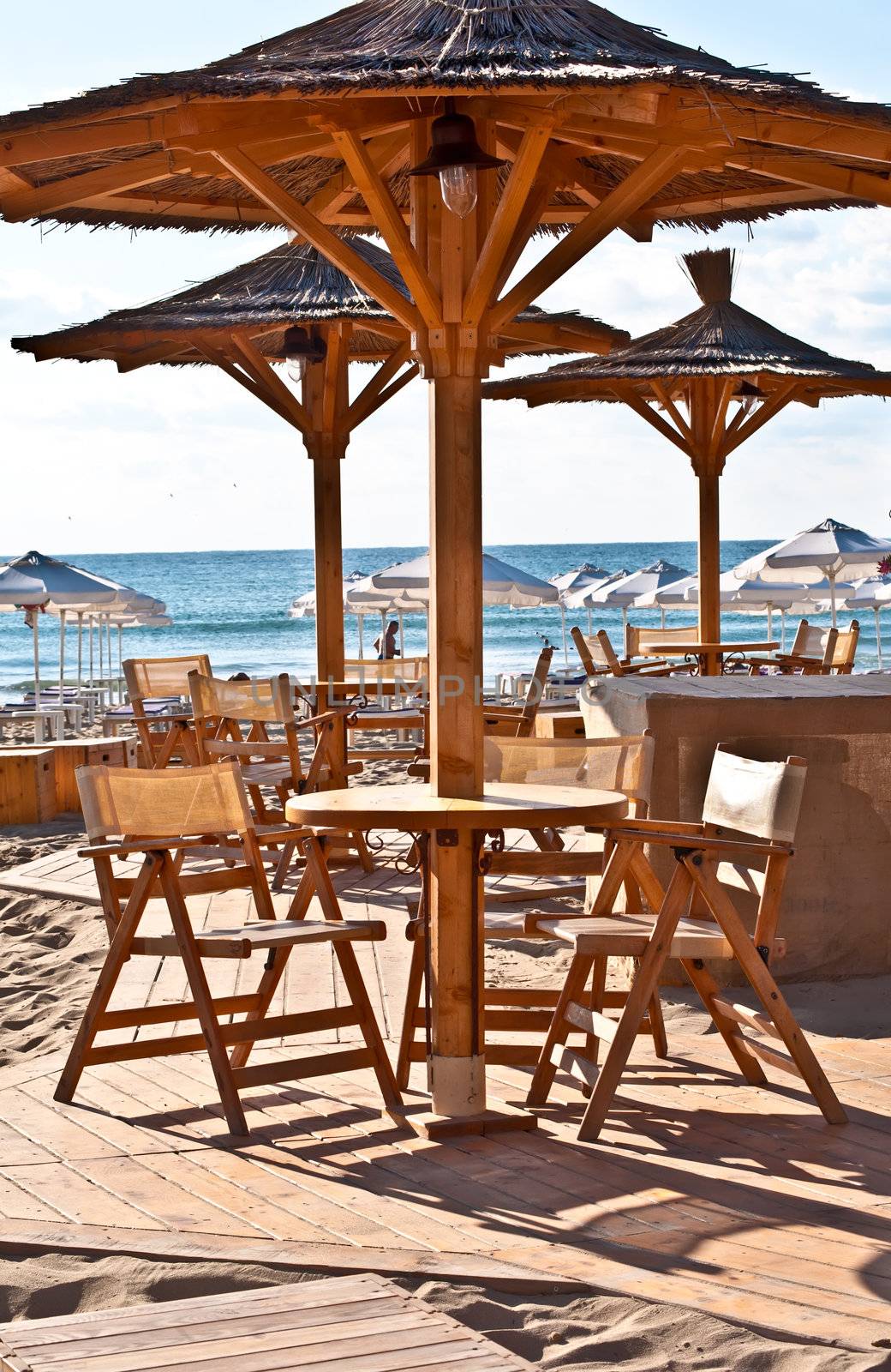 View of the beach with street cafe , table, chair , loungers and umbrellas.