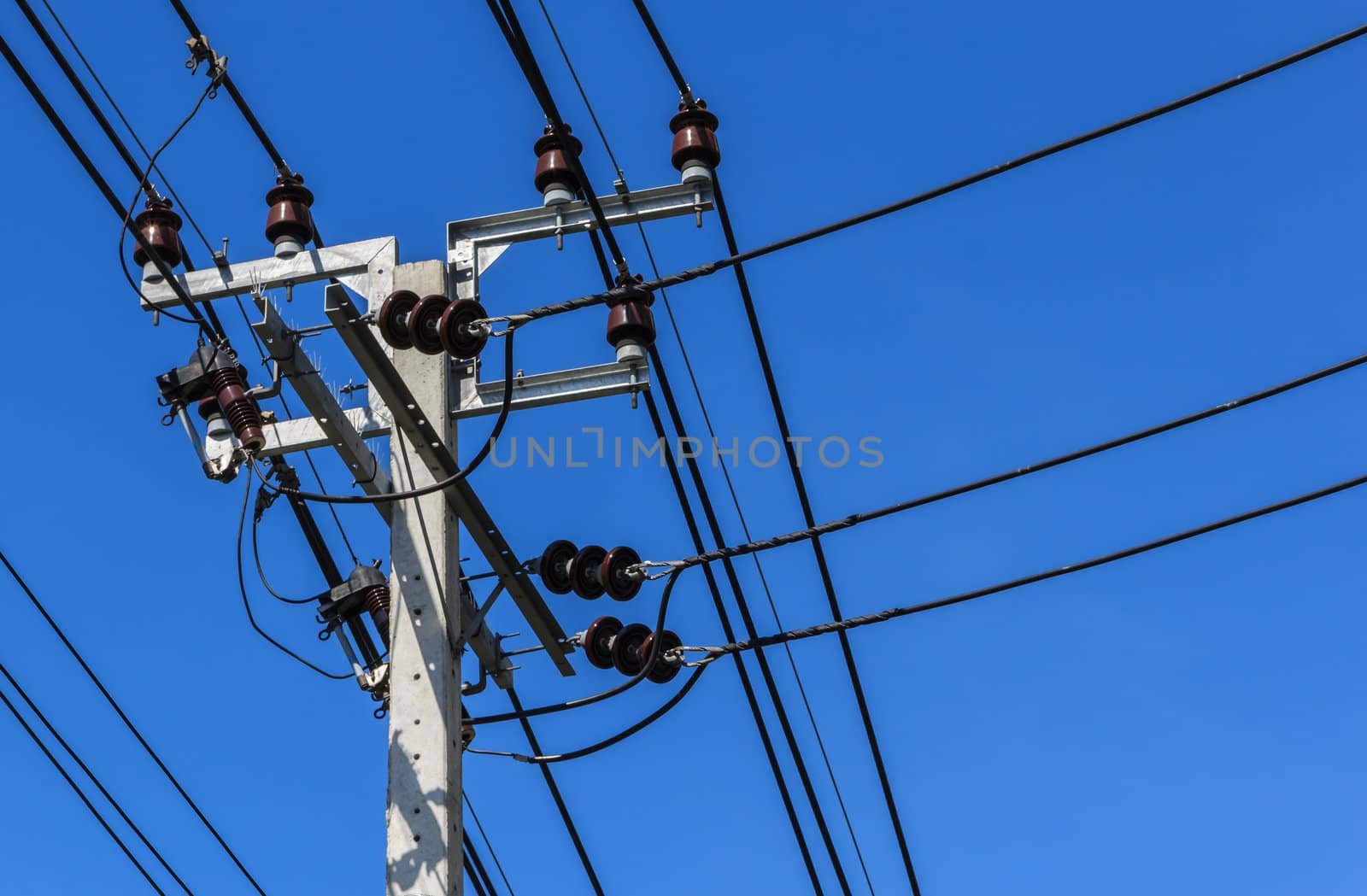 Electric pole with powerlines against bright blue sky.