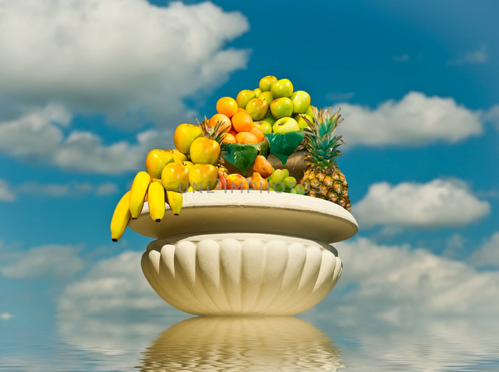 Bowl of fruit on a background of blue sky and water. The symbol of abundance and prosperity.