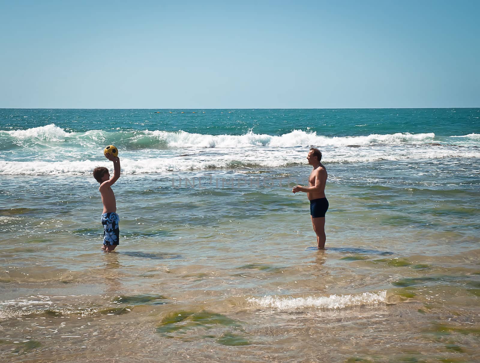 Father and son playing with a ball in the sea .